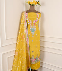 Yellow embroidered saree with floral decorations on a mannequin against a white wall.