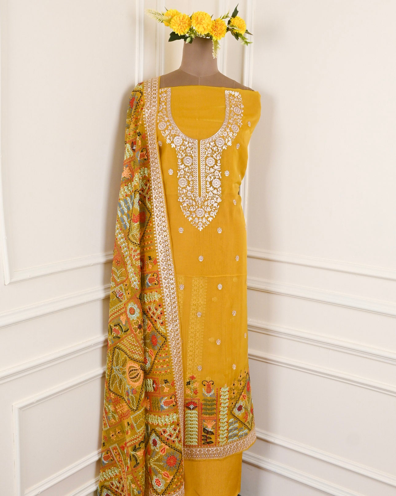 Yellow embroidered dress with a patterned dupatta on a mannequin against a white wall.