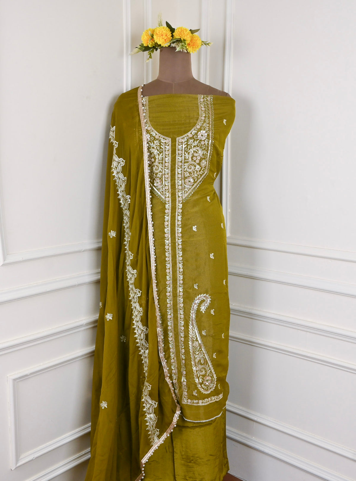Green embroidered dress on a mannequin against a white wall with yellow flowers.
