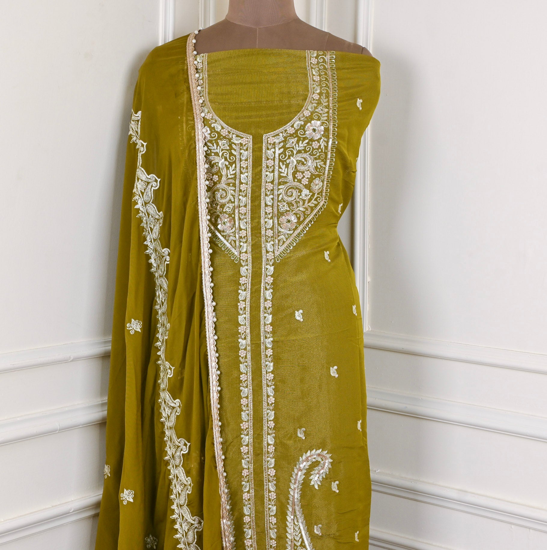 Green dress with white embroidery on a mannequin against a white wall.