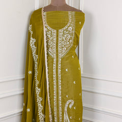 Green dress with white embroidery on a mannequin against a white wall.