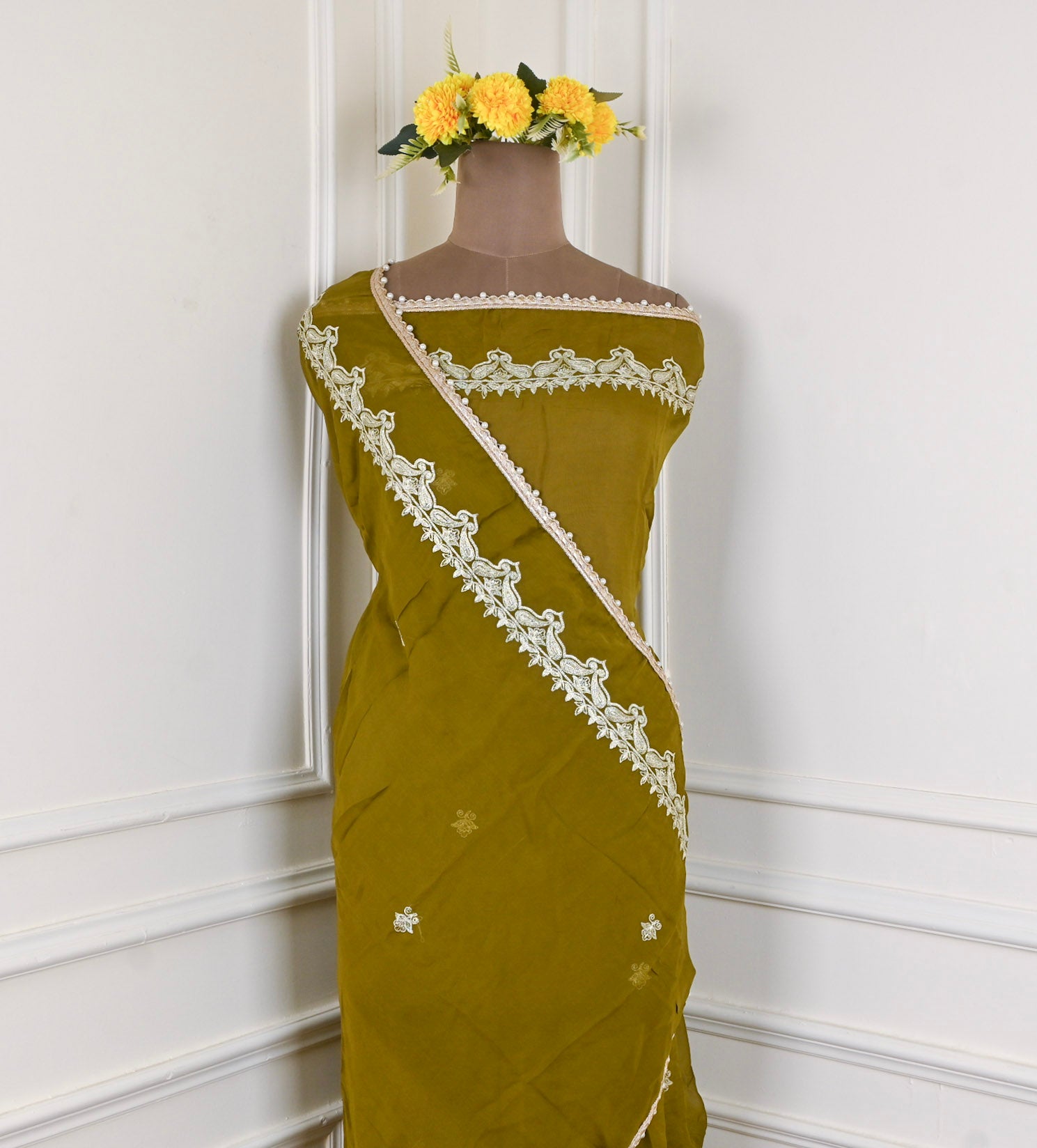 Green saree with white lace on a mannequin against a white wall