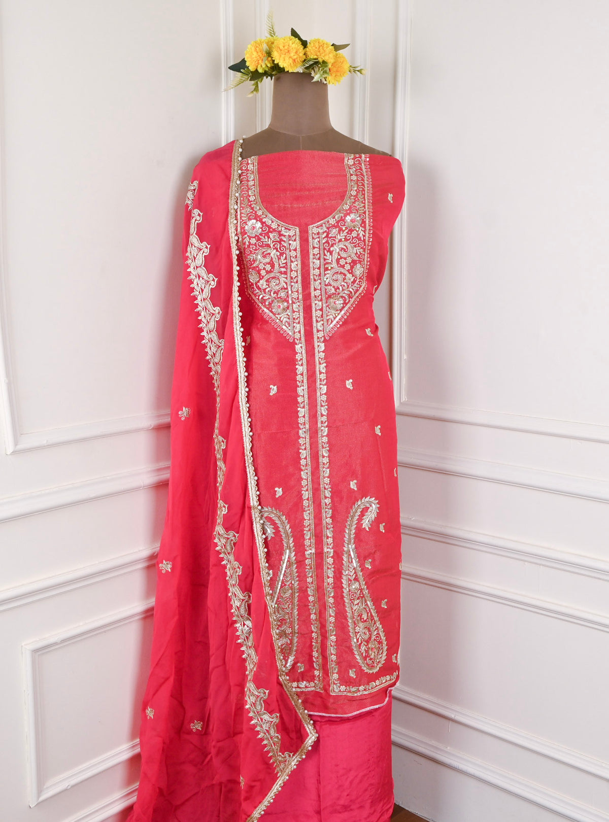 Red embroidered traditional outfit on a mannequin against a white wall.