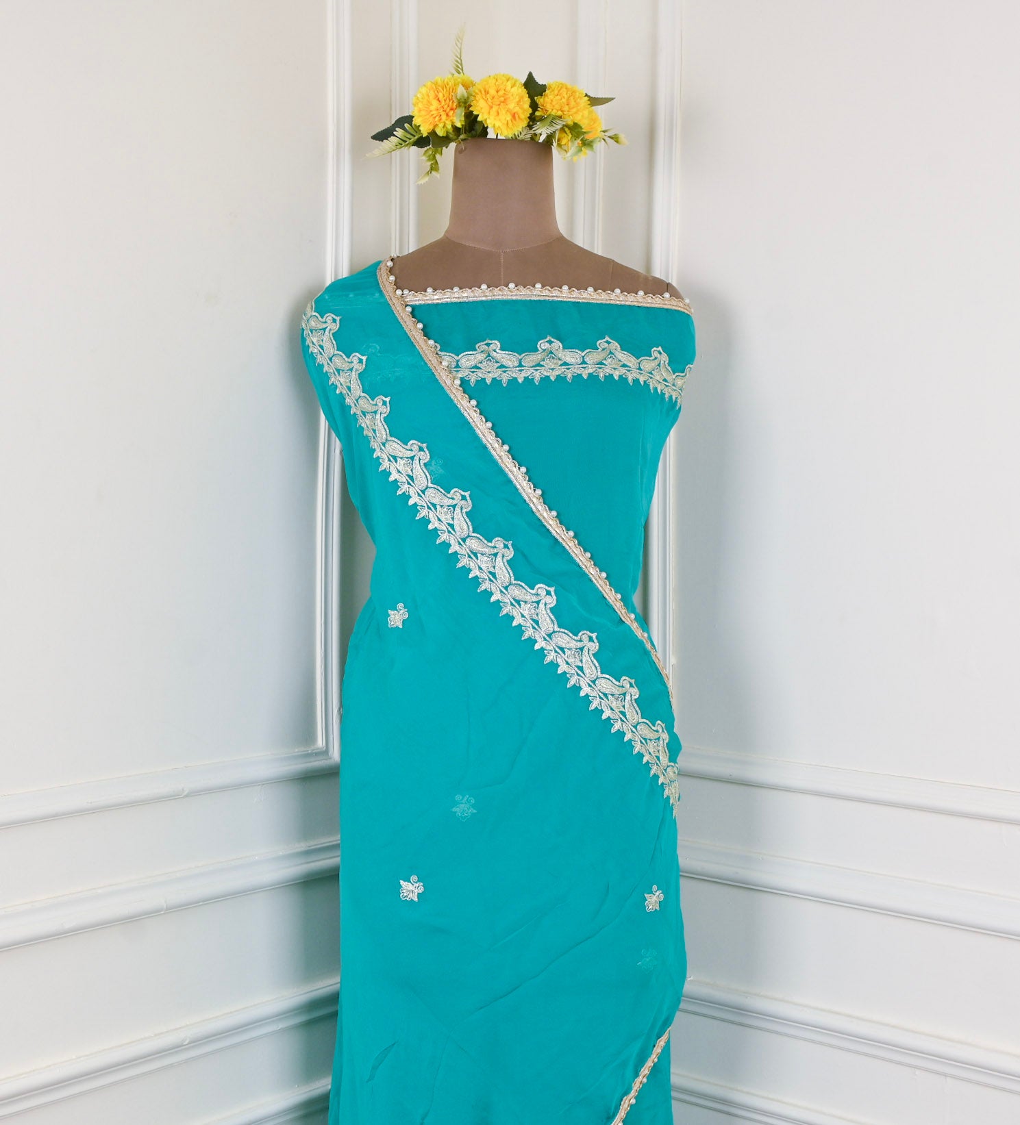 Teal saree with white lace border on a mannequin against a white background